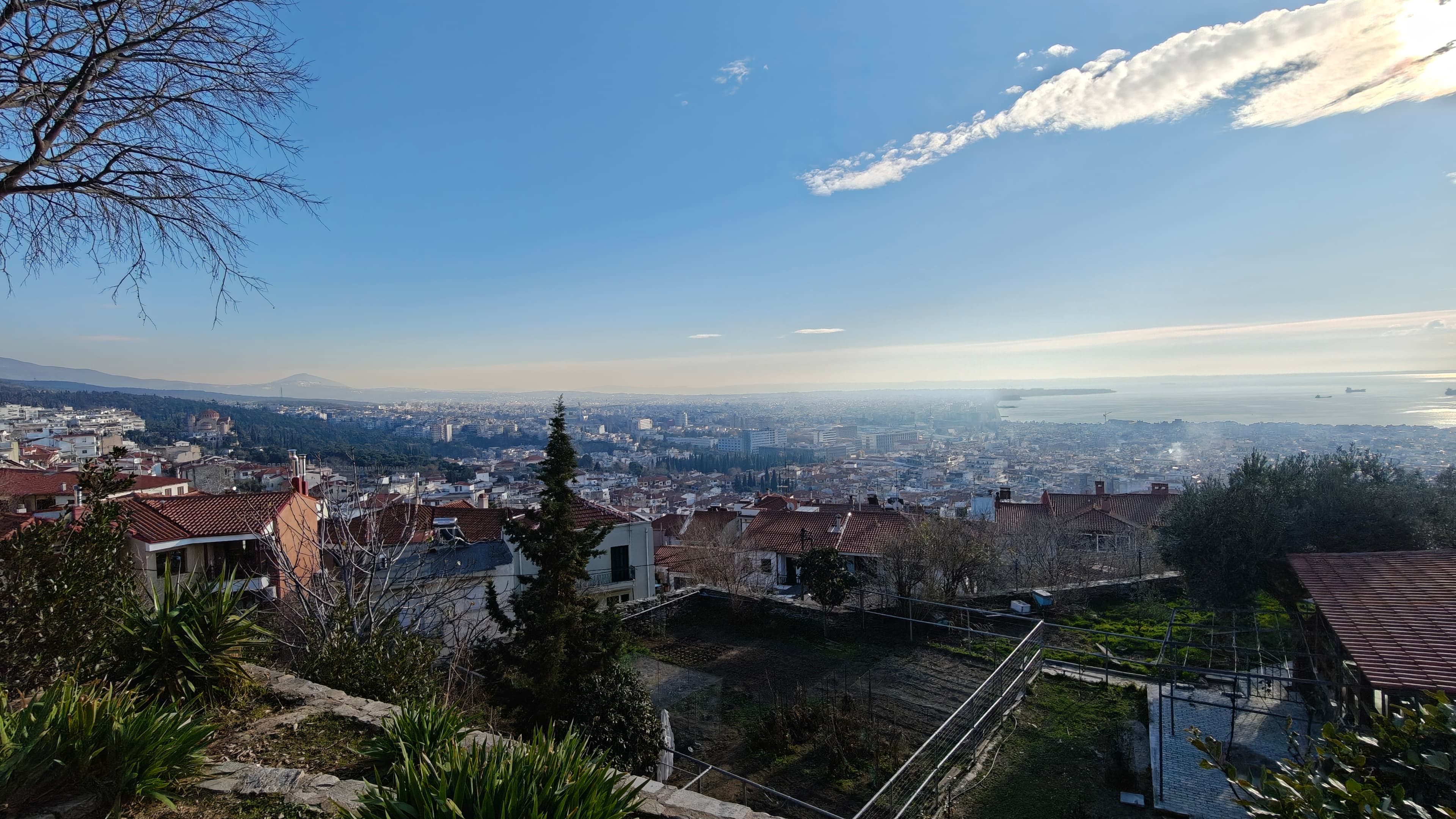 Panoramic view of a coastal city with red-tiled roofs under a clear blue sky.