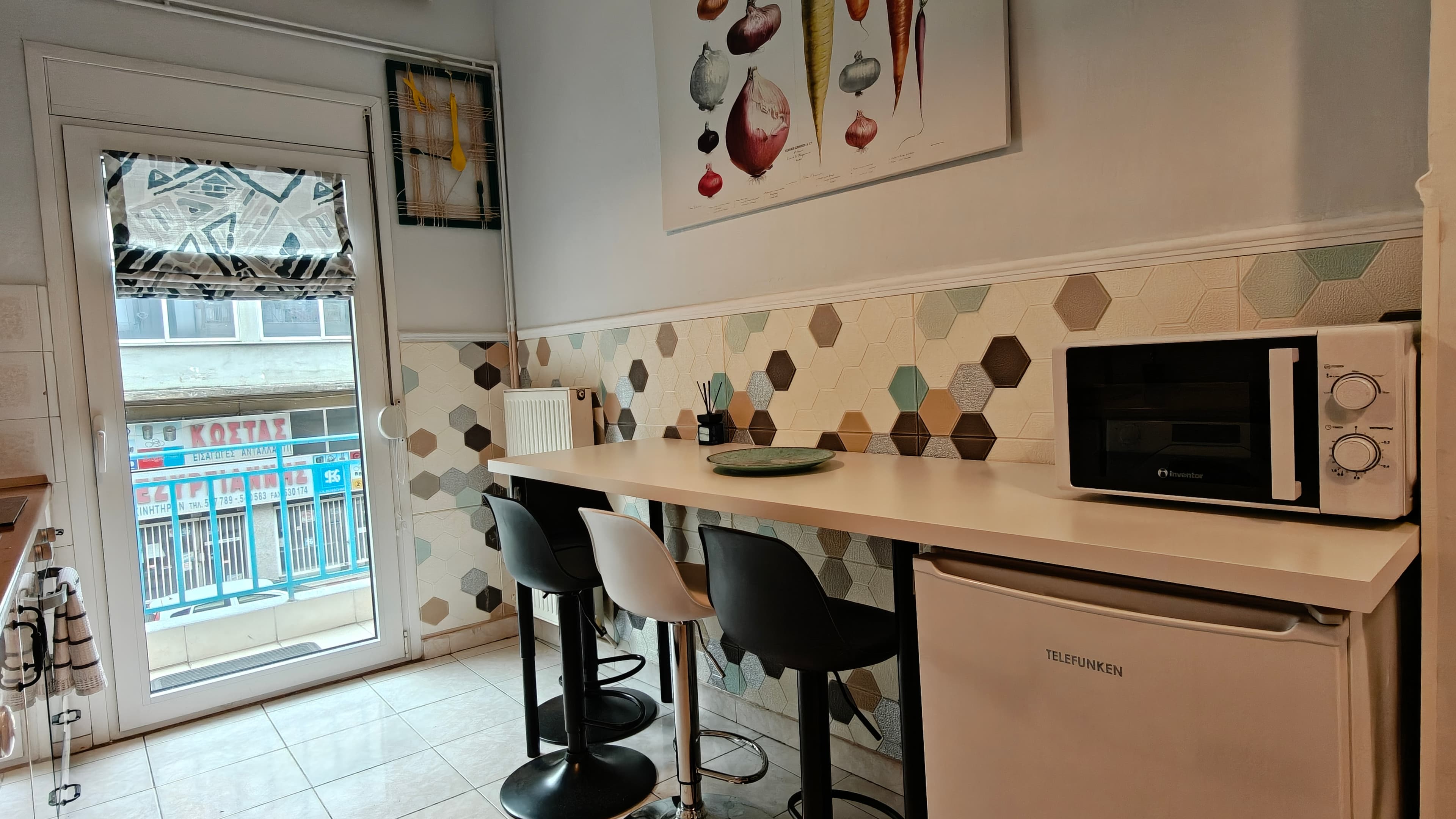 White kitchen counter with bar stools, microwave, and vegetable poster against a hexagonal tiled wall.