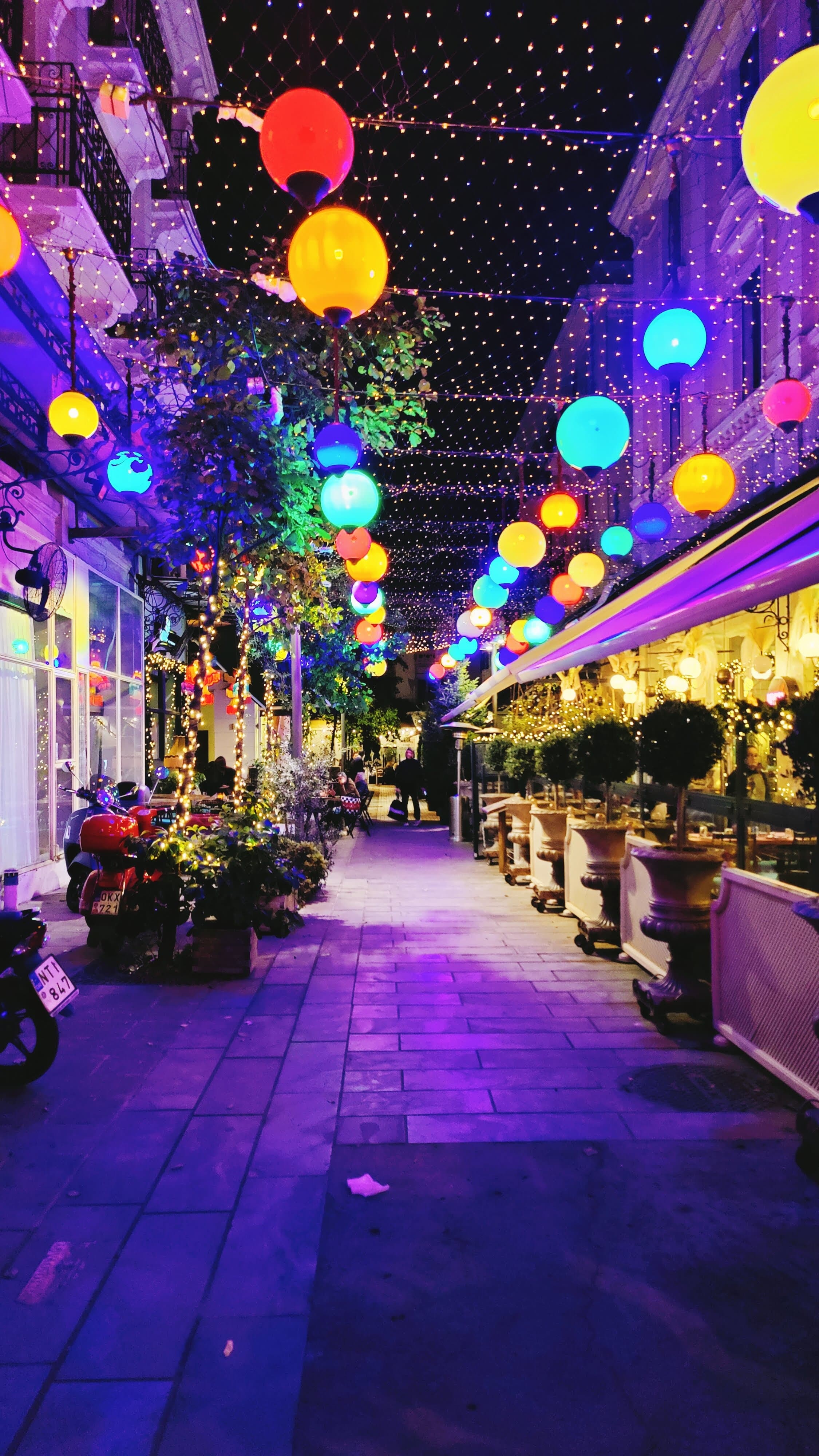 Vibrant night street decorated with colorful spherical lanterns and a canopy of twinkling lights.