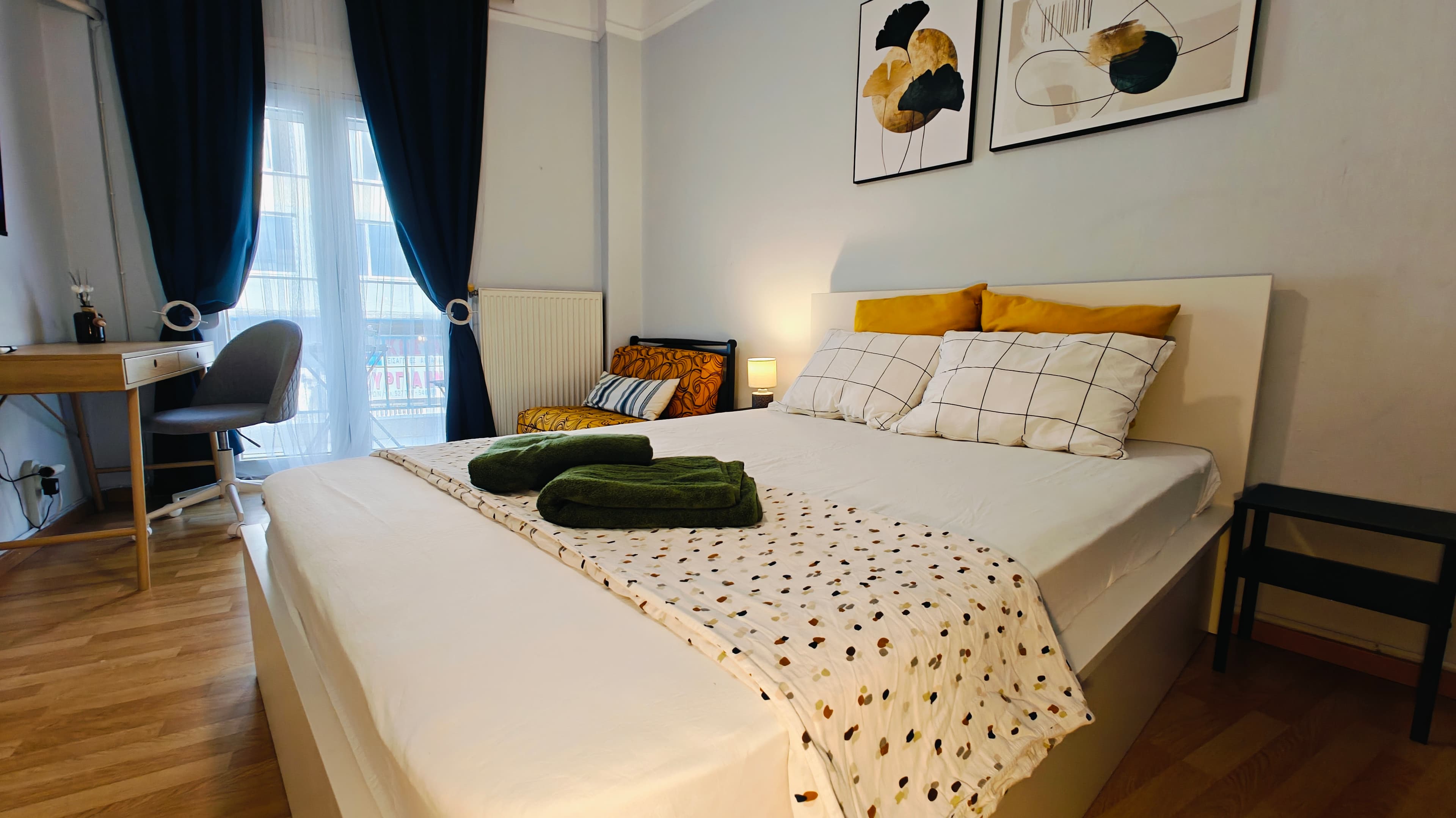 Bright modern bedroom with a white bed, green towels, yellow pillows, and a desk.